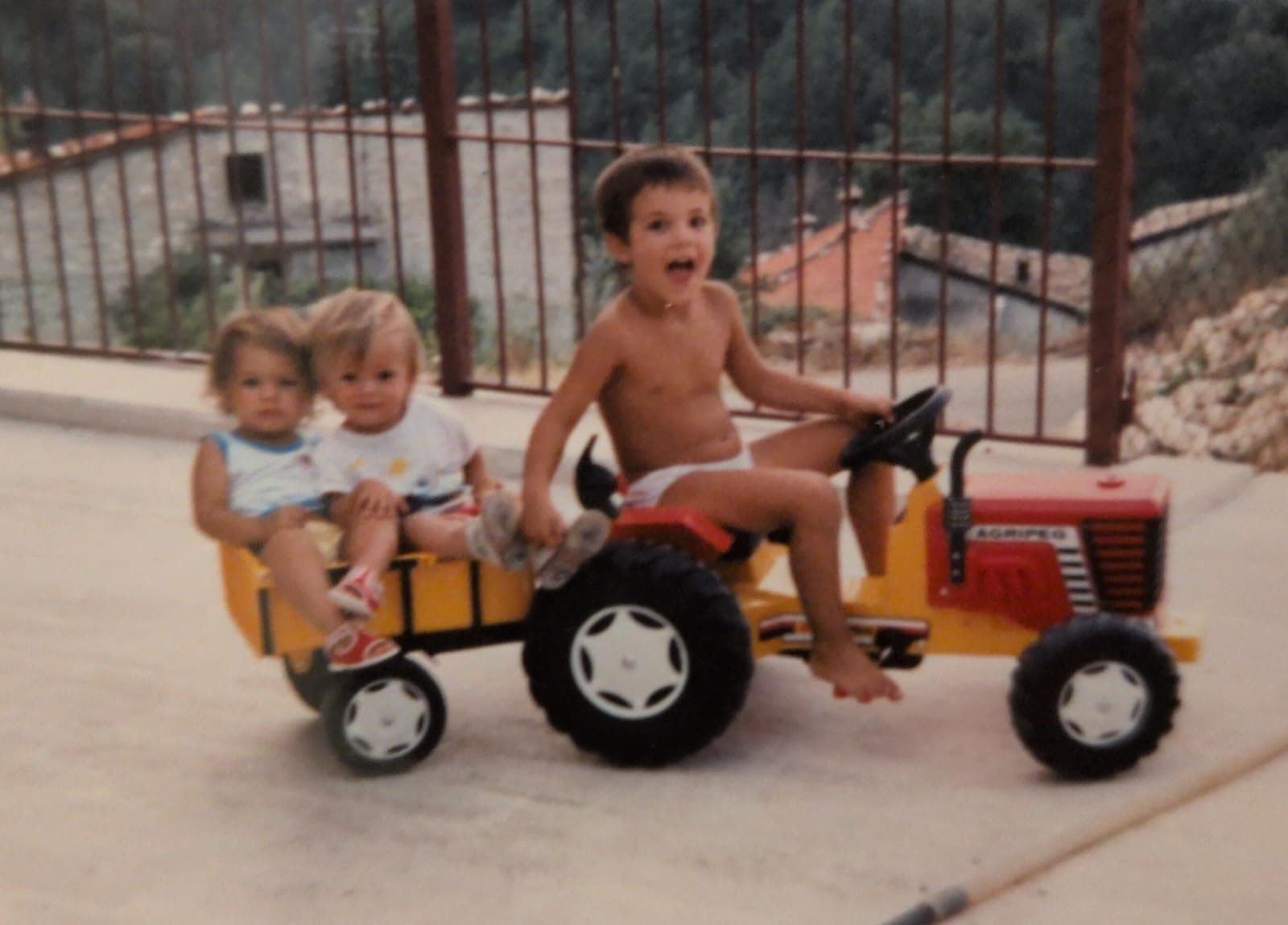 Tre bambini su un trattorino giocattolo nel cortile, nel 1989